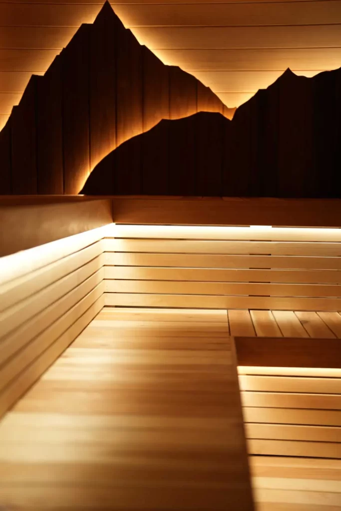 Finnish sauna interior at Fusion Spa & Resort featuring tiered wooden benches, warm ambient lighting, and a sculptural backlit wood wall inspired by natural mountain forms.