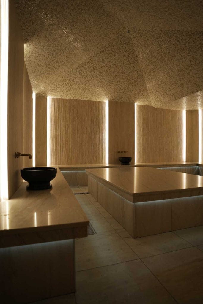 Heated marble hammam wash area at Fusion Spa & Resort featuring smooth stone surfaces, sculpted wash basins, and soft vertical lighting for a calming ritual experience.