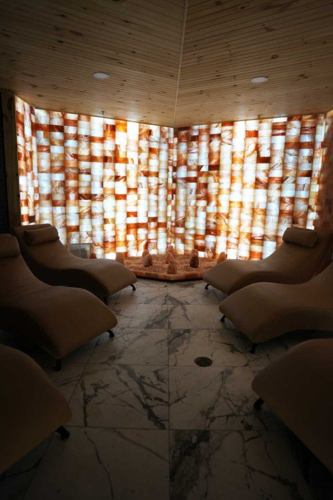 Himalayan salt relaxation lounge at Fusion Spa & Resort featuring illuminated salt block walls, heated salt floor, and ergonomic chaise loungers arranged for quiet rest.