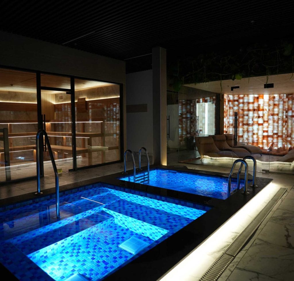 Indoor hydrotherapy pools at Fusion Spa & Resort illuminated with calming blue light, featuring modern stone finishes and adjacent relaxation areas.
