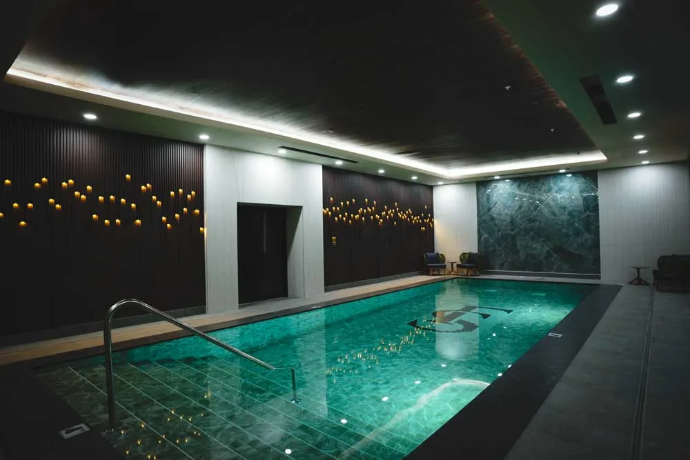 Indoor lap pool at Fusion Spa & Resort featuring emerald-toned water, modern stone finishes, soft ceiling lighting, and candle-inspired wall accents creating a tranquil atmosphere.