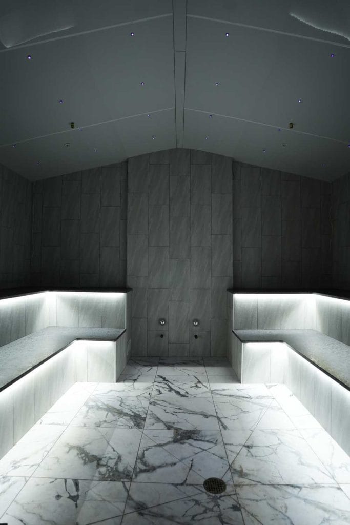 Modern steam room at Fusion Spa & Resort featuring illuminated marble benches, soft indirect lighting, a star-like ceiling, and a refined stone interior designed for deep relaxation.