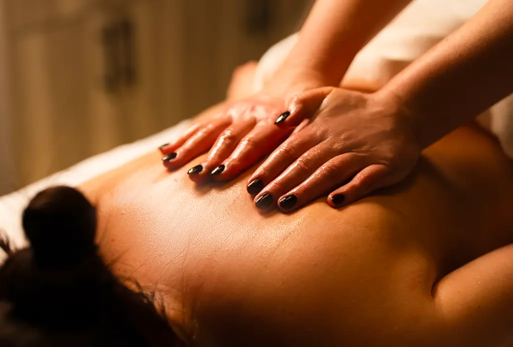 Relaxation Massage Therapy Therapist's hands with dark nail polish massage a person's back during a massage session in warm lighting.