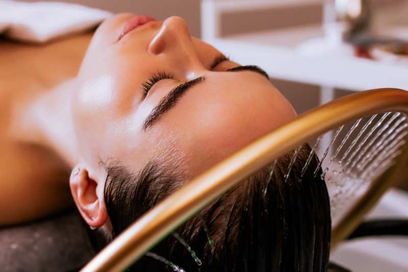 Woman receiving a Japanese head spa scalp massage while water flows through a hair-washing tool over her hair